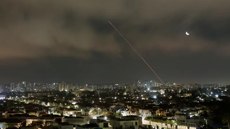 Jejak rudal melintasi langit malam di atas kota, terlihat cahaya ledakan di kejauhan selama serangan Iran-Israel