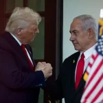 Donald Trump dan Benjamin Netanyahu berjabat tangan di Gedung Putih dengan bendera Amerika Serikat dan Israel di latar belakang