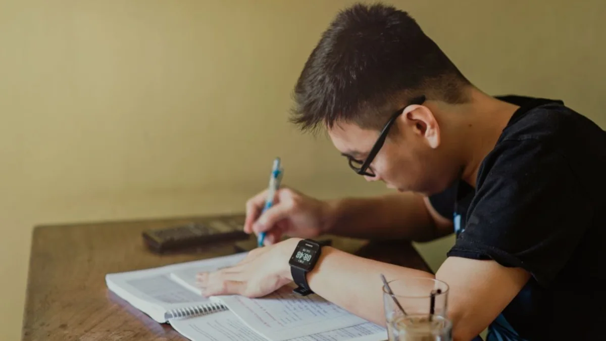 Seorang mahasiswa menulis di buku catatan sambil belajar