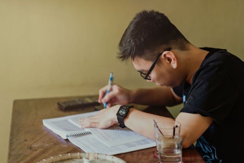 Seorang mahasiswa menulis di buku catatan sambil belajar