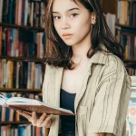 Seorang perempuan muda membaca buku di depan rak toko buku