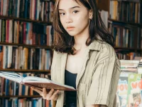 Seorang perempuan muda membaca buku di depan rak toko buku