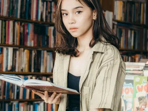 Seorang perempuan muda membaca buku di depan rak toko buku