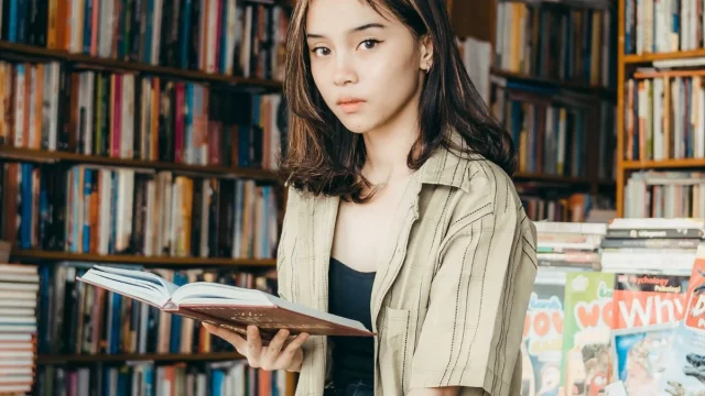 Seorang perempuan muda membaca buku di depan rak toko buku