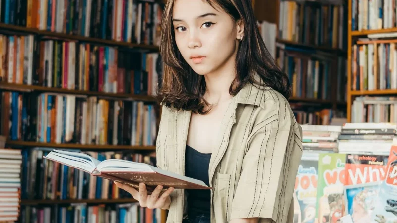 Seorang perempuan muda membaca buku di depan rak toko buku
