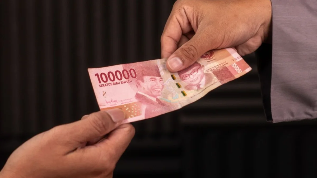 Selembar uang seratus ribu rupiah berpindah dari satu tangan ke tangan lain