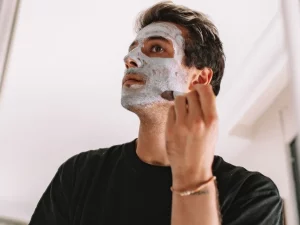 Seorang laki-laki mengoleskan masker perawatan pada wajahnya di depan cermin