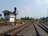 Bangunan rumah sinyal berdiri di tepi rel kereta api dengan tiang sinyal di sampingnya