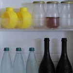 Pintu kulkas terbuka memperlihatkan botol dan wadah makanan di dalamnya