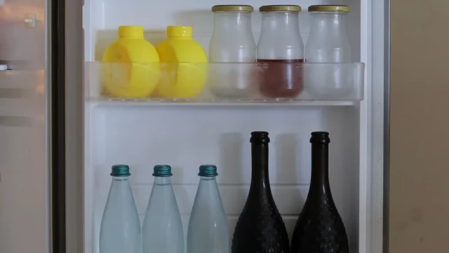 Pintu kulkas terbuka memperlihatkan botol dan wadah makanan di dalamnya