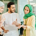 Tiga anak muda muslim berdiskusi sambil membaca berkas di sebuah ruang kerja