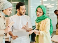 Tiga anak muda muslim berdiskusi sambil membaca berkas di sebuah ruang kerja