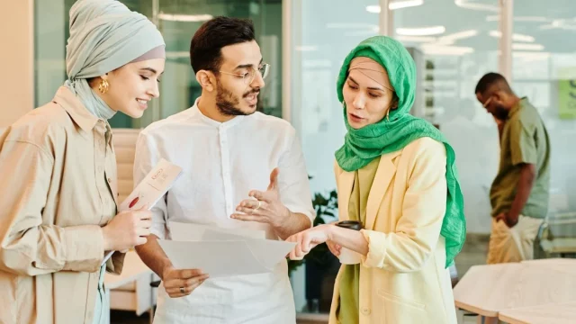 Tiga anak muda muslim berdiskusi sambil membaca berkas di sebuah ruang kerja