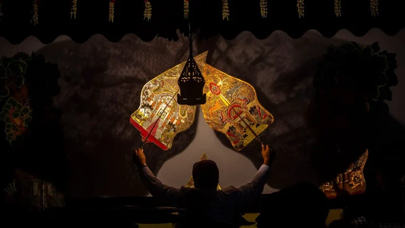 Dalang memainkan wayang kulit di depan kelir dalam sebuah pertunjukan