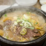 Semangkuk sup daging panas khas Korea dalam mangkuk batu, ditaburi irisan daun bawang