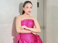 Ayu Ting Ting mengenakan gaun tanpa tali berwarna fuchsia berdiri di lorong studio