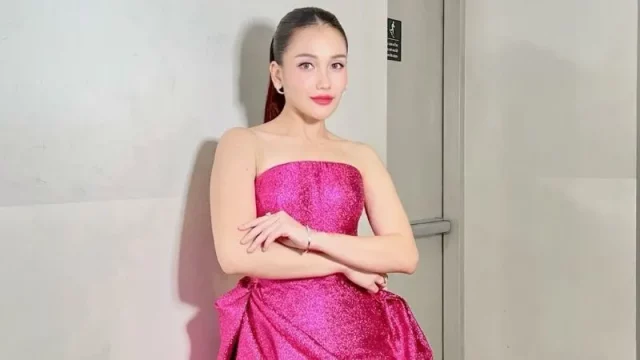Ayu Ting Ting mengenakan gaun tanpa tali berwarna fuchsia berdiri di lorong studio