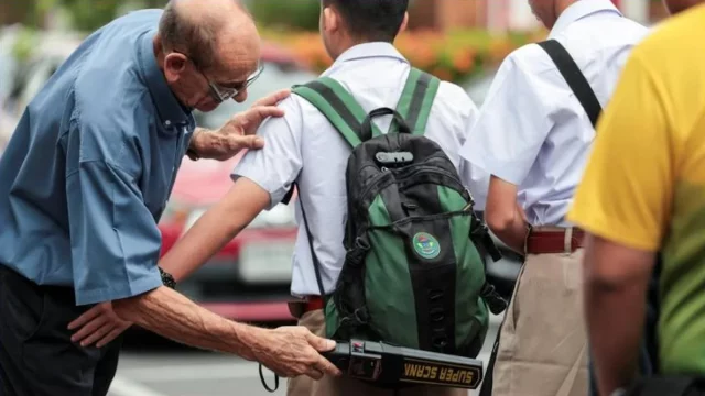 Guru memeriksa tas murid dengan detektor logam di sebuah sekolah di Bangkok