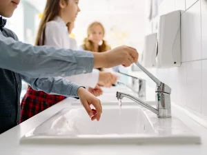 Ilustrasi sejumlah anak berbaris mencuci tangan di deretan wastafel dengan air mengalir dari keran
