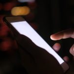 Ilustrasi tangan menggenggam telepon pintar pada malam hari.