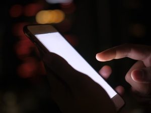 Ilustrasi tangan menggenggam telepon pintar pada malam hari.