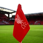 Bendera sudut merah berlambang Liverpool FC dengan latar tribune Stadion Anfield