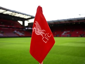 Bendera sudut merah berlambang Liverpool FC dengan latar tribune Stadion Anfield
