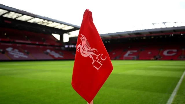 Bendera sudut merah berlambang Liverpool FC dengan latar tribune Stadion Anfield
