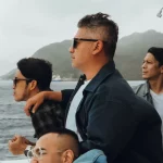 Sejumlah pria berdiri di geladak kapal dengan latar perbukitan dan laut