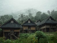 Ilustrasi rumah panggung beratap ijuk di kampung adat Banten dengan hutan berkabut di latar.