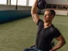 Ilustrasi seorang atlet pengguna kursi roda mengangkat beban kettlebell dengan satu tangan di ruang latihan