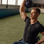Ilustrasi seorang atlet pengguna kursi roda mengangkat beban kettlebell dengan satu tangan di ruang latihan