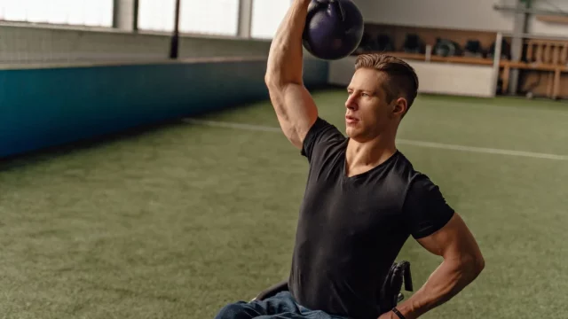 Ilustrasi seorang atlet pengguna kursi roda mengangkat beban kettlebell dengan satu tangan di ruang latihan