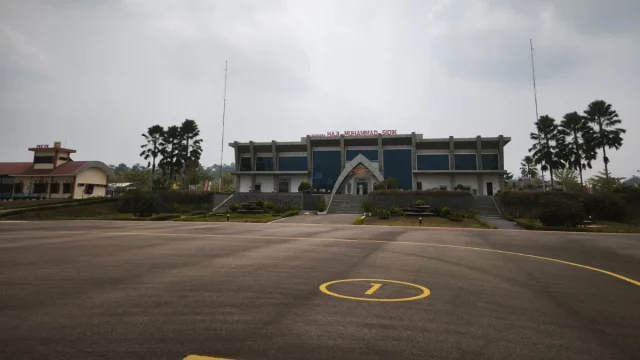 Gedung terminal Bandara Haji Muhammad Sidik dengan langit berkabut asap dan apron yang lengang.