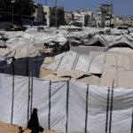 Seorang perempuan Palestina dan seorang anak berjalan di samping deretan tenda pengungsian