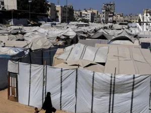 Seorang perempuan Palestina dan seorang anak berjalan di samping deretan tenda pengungsian