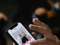 Tangan memegang ponsel pintar yang menampilkan kartu profil sebuah aplikasi kencan