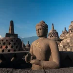 Arca Buddha dan deretan stupa berlubang di teras atas Candi Borobudur dengan latar langit biru dan perbukitan