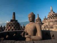 Arca Buddha dan deretan stupa berlubang di teras atas Candi Borobudur dengan latar langit biru dan perbukitan