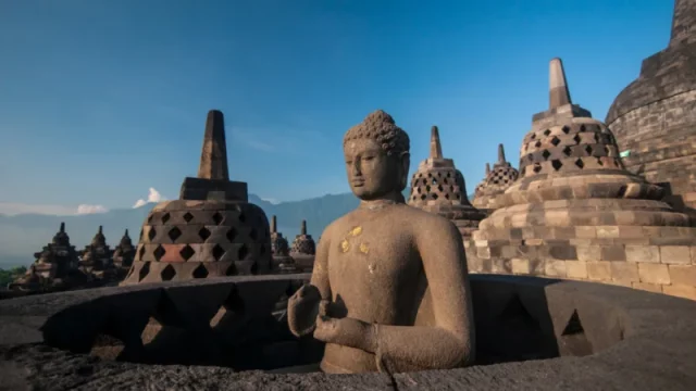 Arca Buddha dan deretan stupa berlubang di teras atas Candi Borobudur dengan latar langit biru dan perbukitan