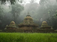Kompleks stupa bata tua berlumut berdiri di padang rumput yang dikelilingi hutan tropis berkabut