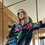 Celine Dion mengenakan busana bermotif warna-warni berpose di depan cermin