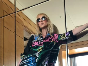 Celine Dion mengenakan busana bermotif warna-warni berpose di depan cermin