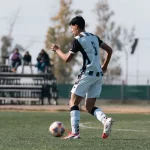 Pesepak bola menggiring bola di lapangan hijau
