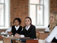 Tiga siswa berseragam sekolah menengah duduk di meja ruang kelas berdinding bata