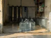 Deretan galon bening dan tabung penyaring baja di sebuah depot air minum isi ulang.