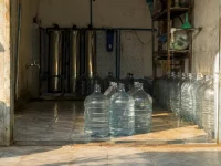 Deretan galon bening dan tabung penyaring baja di sebuah depot air minum isi ulang.
