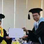 Seorang doktor baru bertoga menerima map penghargaan dari pimpinan sidang dalam ujian terbuka di ruang sidang kampus