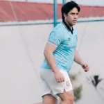 El Rumi berkaus biru muda menggiring bola di lapangan berumput sintetis