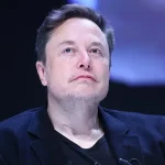 Elon Musk mengenakan jas hitam menatap ke atas dalam sebuah acara